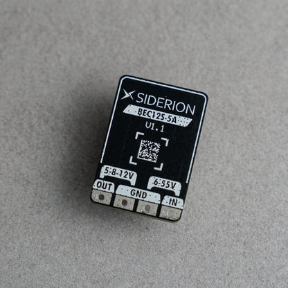 A small black electronic component with white printed text and silver metal pins, photographed on a textured light gray surface. The brand name SIDERION is clearly visible on the top surface.