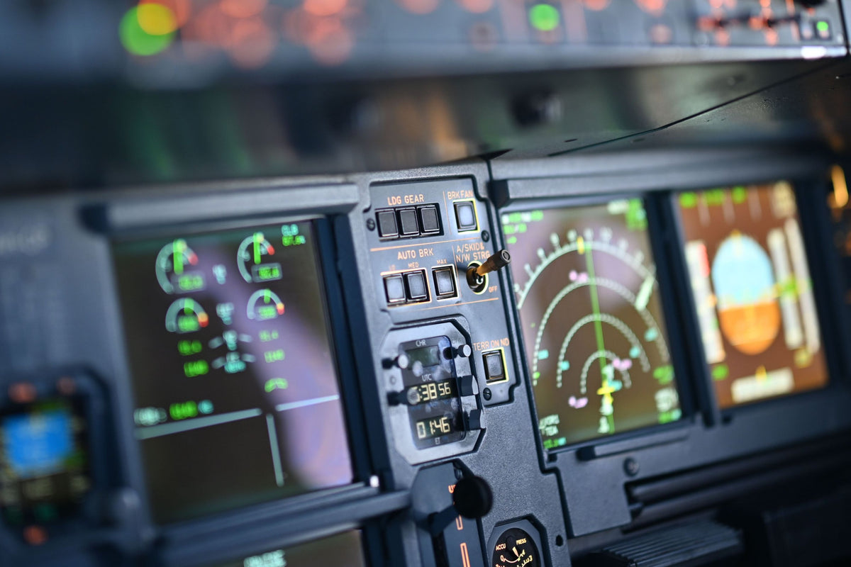 Close-up of an aircraft cockpit instrument panel with illuminated screens and control displays, photographed in a real environment with shallow depth of field.