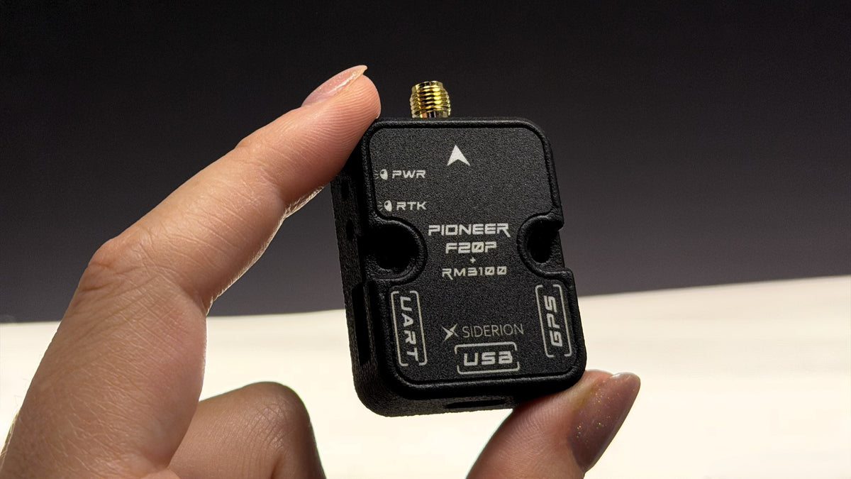 A hand holding a small black Pioneer F20P GPS receiver module with a gold-plated connector, against a dark and light background.